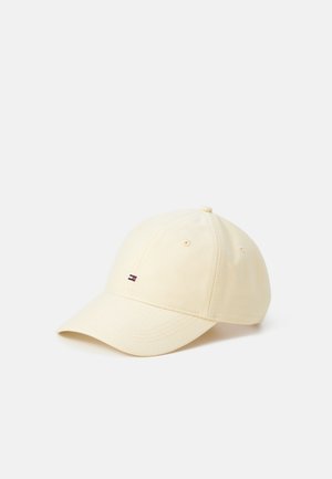 Casquette de baseball beige clair avec une visière incurvée et un petit logo de drapeau rouge, blanc et bleu sur le panneau avant central, présentée sur fond blanc.