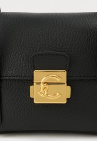 Bolso de cuero negro con textura y un cierre rectangular dorado brillante que presenta un diseño estilizado de "C" entrelazadas.