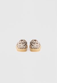 Vue arrière des chaussures présentant un dessus en tissu beige à motif avec des accents marron, un bout arrondi et une semelle en caoutchouc beige clair.