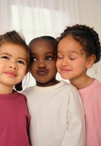 Kolm last kannavad pikkade varrukatega, ümarate kaelustega t-särke roosade, beežide ja lillas toonides. Riie näeb välja pehme ning sobib vabalt selga.