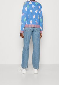 Lys blå sweater med farverige mønstre, ribbede manchetter og kant. Kombinationen er med lige ben blå jeans og hvide platform sneakers.