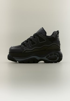 Schwarzer klobiger Sneaker mit dicker, strukturierter Sohle, Schnürung vorne und gepolstertem Kragen, seitlich auf neutralem Hintergrund gezeigt.