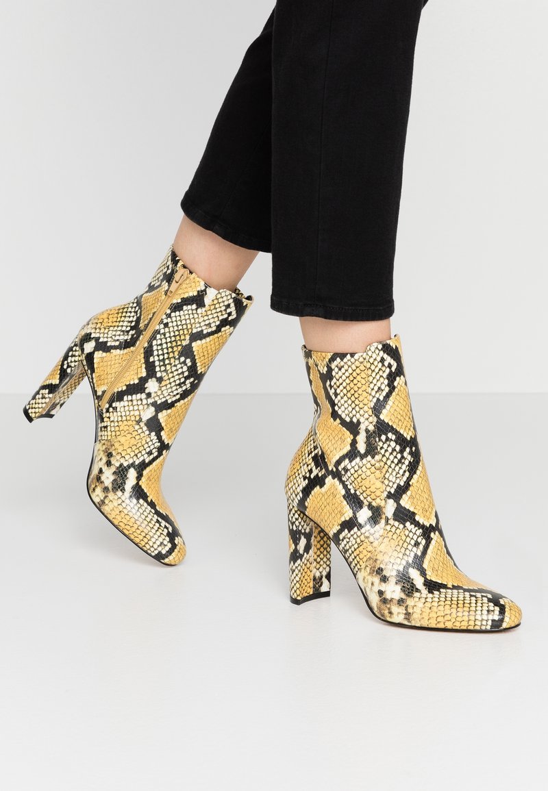 Bottes cheville à imprimé serpent jaune et noir avec un bout pointu et un talon haut épais, dotées d'une fermeture éclair latérale et d'une finition texturée.