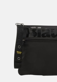 Borsa a spalla nera in materiale nylon testurizzato, con un logo prominente, chiusura con zip e una tracolla con dettagli in metallo e branding.