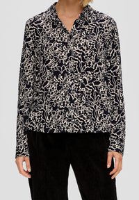 Camicia blu navy con motivo floreale bianco, maniche lunghe e colletto. Realizzata in tessuto leggero. Da abbinare a pantaloni neri texturizzati.