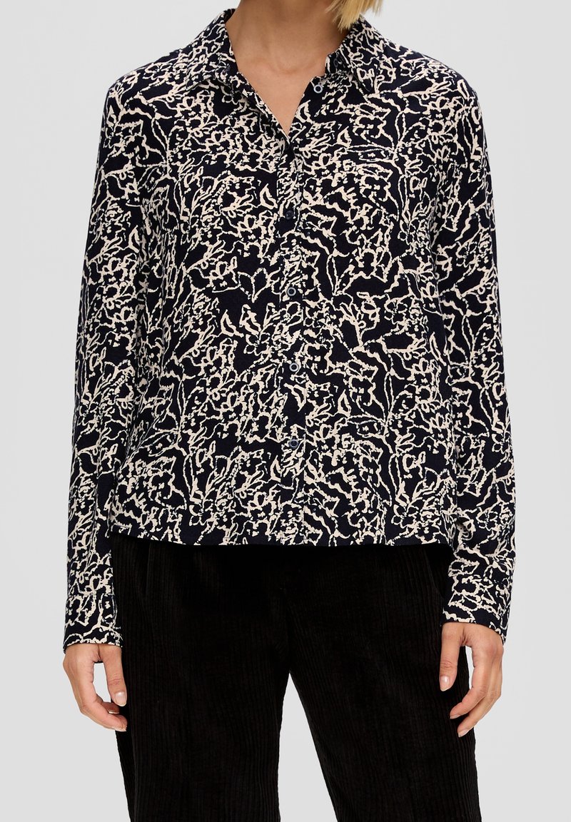 Camicia blu navy con motivo floreale bianco, maniche lunghe e colletto. Realizzata in tessuto leggero. Da abbinare a pantaloni neri texturizzati.