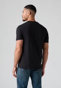 Fekete rövid ujjú, kerek nyakú pamut póló, hátulról nézve, kék farmernadrággal párosítva. Simaságú anyag.