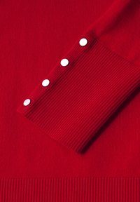 Roter Strickpullover mit gerippter Textur und vier weißen KnopfAkzenten an den Ärmeln. Klassischer Rundhalsausschnitt und taillierte Passform.