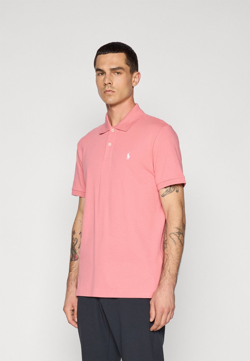 Camisa polo rosa com gola, com abertura de dois botões e logotipo bordado. Mangas curtas, corte regular e tecido de algodão.
