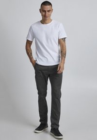 Hvit bomull t-skjorte kombinert med grå slim-fit bomullsbukser. Sorte joggesko med hvite såler. Enkel, uformell og tettsittende design.