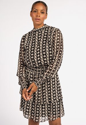 Zwart en crèmekleurige patroondress met hoge hals, lange mouwen en elastische tailleband. Bevat gerimpelde accenten op de mouwen en de zoom.