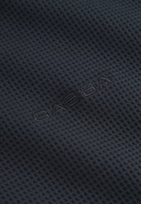 Čierna textúrovaná tkanina so vzorom mriežky, obsahujúca jemné vyrazené logo „GABBA“ v čiernej farbe. Hladká textúra s priedušným pocitom.