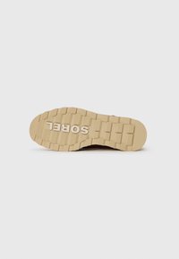 Suela de zapatilla SOREL con un diseño de goma texturada en color marrón claro. Presenta patrones rectangulares y el nombre de la marca grabado en el centro.