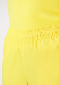 Pantalones cortos deportivos amarillos con una tela suave y elástica y una cinturilla elástica para mayor comodidad. Sin patrones visibles ni detalles de hardware.