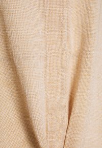 Tessuto beige chiaro con un motivo intrecciato testurizzato, caratterizzato da un sottile design a griglia. Aspetto morbido e leggermente trasparente.