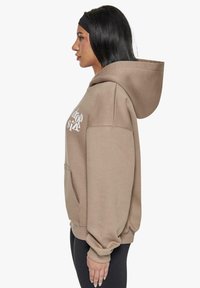 Beige Kapuzenpullover mit großer Kapuze, lockerer Passform und Kängurutasche. Der Text lautet "drop size" in Weiß. Gerippte Bündchen und Saum sorgen für Komfort.