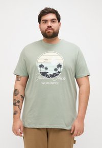 Lysegrøn t-shirt lavet af blødt bomuld, med et cirkulært grafisk motiv af palmetræer, en solnedgang, og teksten "Jack & Jones WORLDWIDE."