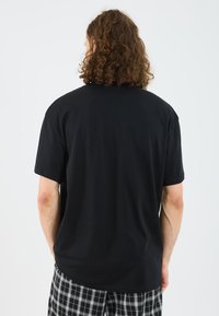T-shirt noir à manches courtes avec une coupe décontractée, en coton, avec un dos uni. Associé à un pantalon à carreaux à motifs.