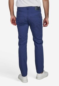 Blauwe katoenen broeken met een slim fit, voorzien van twee achterzakken, subtiele stiksels en gedragen met witte sneakers.