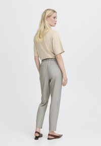 Béžové tričko s krátkým rukávem, šedé zúžené kalhoty s elastickým pasem, bočními kapsami a hnědé baleríny. Hladká textura a čisté linie.