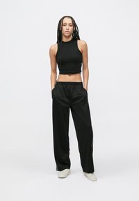 Čierny krátky tank top v kombinácii s čiernymi voľnými nohavicami so bočnými vreckami a bielymi pruhmi ako akcent. Textúrovaná látka, ležérny dizajn.