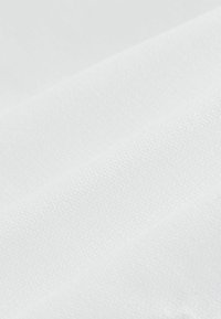 Valkoinen kangas, jossa on teksturoitu pinta, järjestetty laskoksiin. Kudontamalli on näkyvissä, mikä vihjaa kevyestä ja hengittävästä materiaalista.