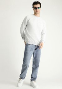 Sudadera gris de cuello redondo con mangas largas, combinada con jeans de denim azul claro y zapatillas blancas. Los accesorios incluyen gafas de sol con tintado verde.