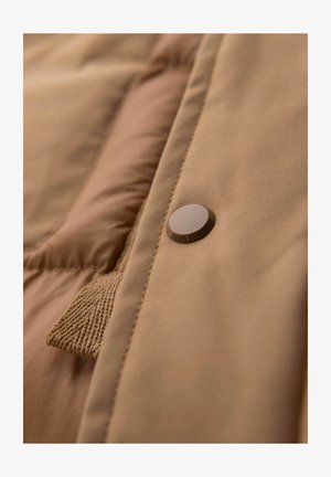 Tissu de veste doudoune beige avec une texture lisse, comportant un bouton pression marron marqué "OMBREWEAR" et une étiquette tissée sur le côté.