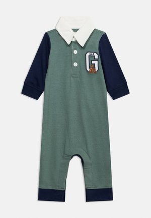 Combinaison bébé à manches longues verte avec manches et poignets bleu marine, col blanc, deux boutons et un écusson avec la lettre G et un petit ours.