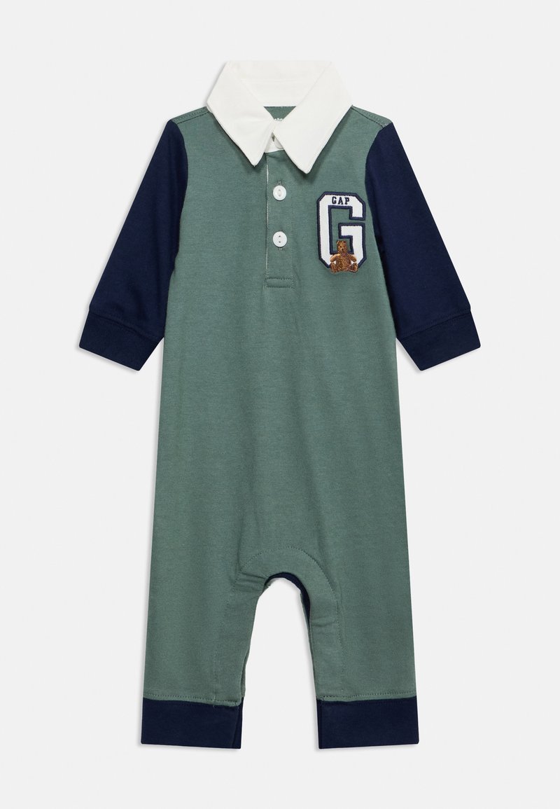 Combinaison bébé à manches longues verte avec manches et poignets bleu marine, col blanc, deux boutons et un écusson avec la lettre G et un petit ours.