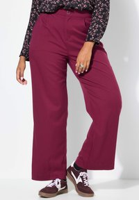 Bordeaux brede pantalon gemaakt van gladde stof, met een sluiting met een knoop aan de voorkant en gecombineerd met bruin-witte sneakers.