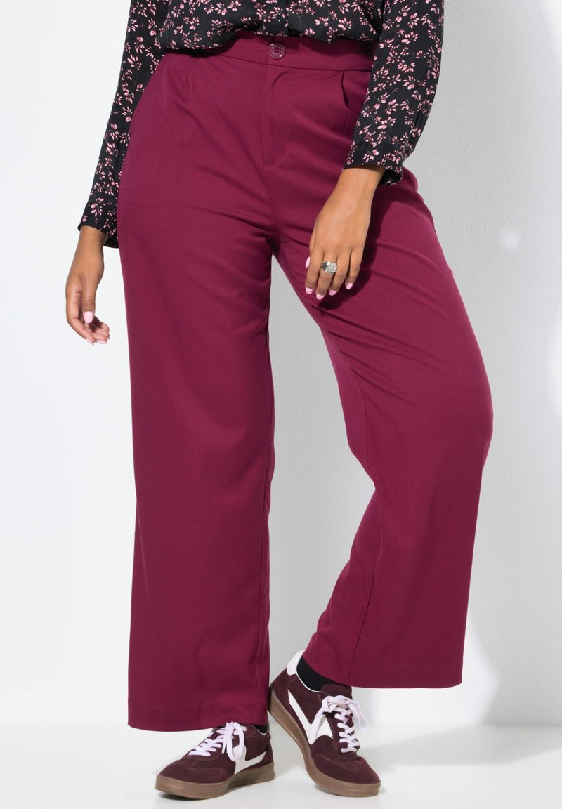 Bordeaux brede pantalon gemaakt van gladde stof, met een sluiting met een knoop aan de voorkant en gecombineerd met bruin-witte sneakers.
