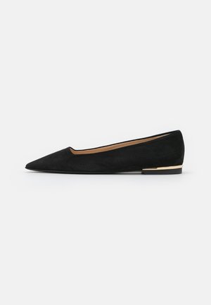 Chaussure plate en daim noir à bout pointu avec un petit talon et un subtil accent doré sur le talon, montrée de profil sur un fond uni.