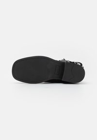 Black rubber shoe sole with a textured pattern, featuring a rounded shape and clean lines. Includes a logo embossed on the sole.
