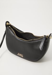 Black leather handbag with gold hardware, zip closure, and a curved shape. Features a logo on the front and a detachable strap.