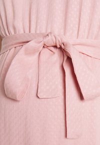 Vestido de tecido rosa com um padrão texturizado, apresentando um cinto amarrado na cintura feito do mesmo material. Textura suave e cor delicada.