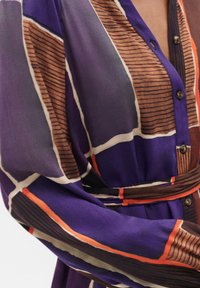 Abito viola a motivi con un mix di righe verticali e orizzontali, con una chiusura a bottoni nella parte anteriore e una cintura in vita. Tessuto liscio.