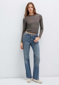 Top grigio a maniche lunghe con coste abbinato a jeans dritti azzurri chiari, con cinque tasche e leggere sfumature. Modello che indossa sneakers beige.