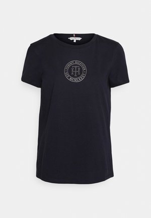 Czarny t-shirt z krótkim rękawem i okrągłym dekoltem, z okrągłym logo Tommy Hilfiger i napisem na środku klatki piersiowej.