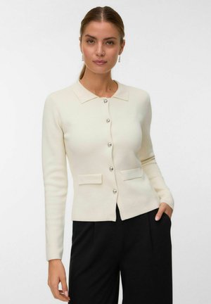 Cardigan ajusté beige clair avec col, six boutons brillants et deux poches avant. Manches longues avec poignets côtelés, fabriqué en textile doux.