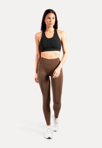 Zwarte sportbeha met een gestructureerd ontwerp en een onderborstband, gecombineerd met bruine leggings met hoge taille en een zijzak.