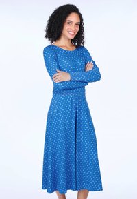 Blaues Kleid mit Punkten, langen Ärmeln, Rundhalsausschnitt und gerafftem Taillenbereich. Aus weichem Stoff gefertigt, mittellang bis zur Wade und mit seitlichen Taschen.