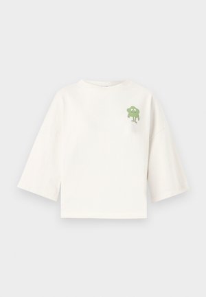 Tricou alb din bumbac, cu un design scurt, având mâneci trei sferturi și un personaj de desene animate verde tipărit pe piept.