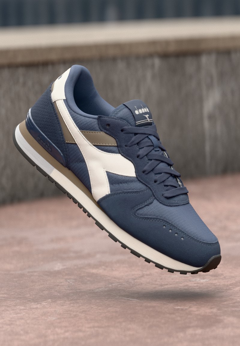 Navy and white athletic shoe with a textured fabric upper, round toe, and a durable rubber sole. Features mesh panels and lace-up front.