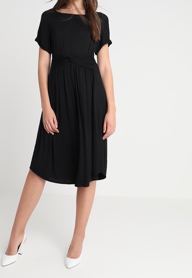 Musta polvipituinen mekko pehmeästä kankaasta, jossa on lyhyet hihat, kerätty vyötärökoristelu ja rento leikkaus. Yhdistetty valkoisiin kärjetön korkokenkiin.