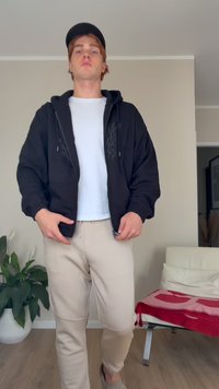 Casaco de hoodies preto com um design texturizado, t-shirt branca por baixo e calças de moletom beges. Estilo urbano casual com um corte descontraído.