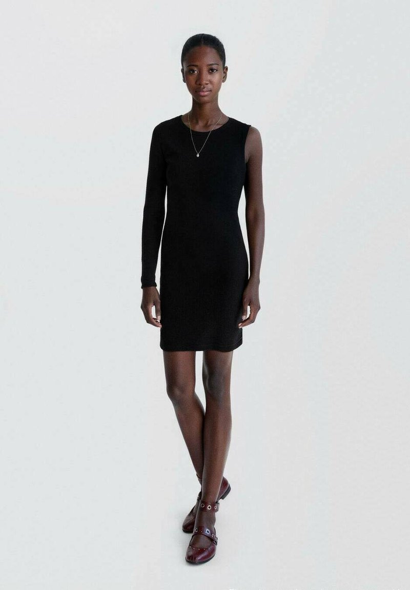 Robe noire côtelée avec une manche longue, design ajusté. Associée à des chaussures rouge foncé avec des accents ronds et des brides de cheville.
