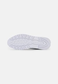 Semelle d'une basket blanche Reebok montrant des grips circulaires, des rainures et le logo Reebok embossé près du centre.