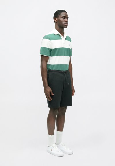 Svītrains zaļš un balts polo krekls, melni šorti, baltas kurpes un gaišas zeķes. Iezīmējas ar apkakli un aukliņu jostā.