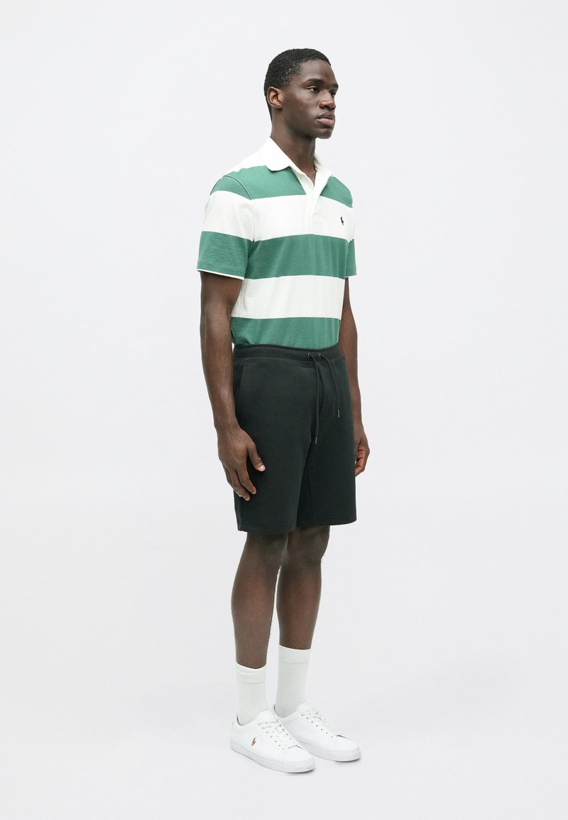 Polo a righe verdi e bianche, pantaloni corti neri, scarpe bianche e calze chiare. Presenta un colletto e una vita con cordoncino.